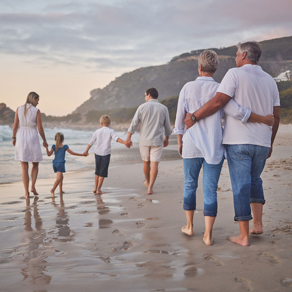 Family, generations and back with walking, beach and sunset with men, women and children with love. Parents, grandparents and kids by ocean, holding hands and bond on summer vacation with solidarity.